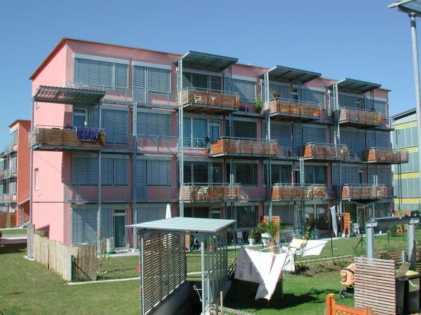 Rotes Mehrfamilienhaus mit zahlreichen Fenstern, Balkonen und einem Garten
