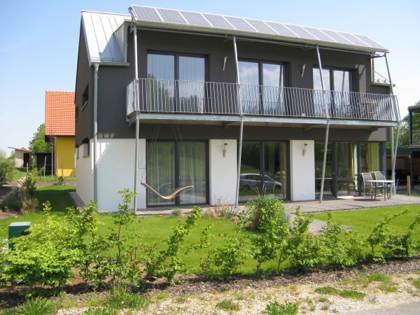 Grau-weißes Passivhaus mit Giebeldach, Solarzellen und dazugehörigem Garten
