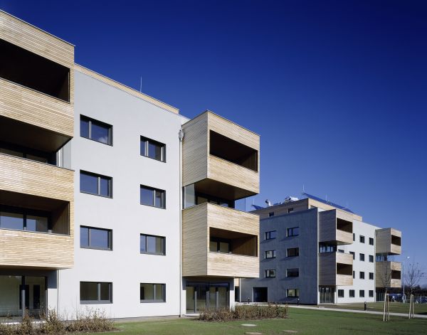 Würfelförmiges Passivhaus mit überdachten Balkonen an jeder Ecke der vier Stockwerke und Solarzellen am Dach