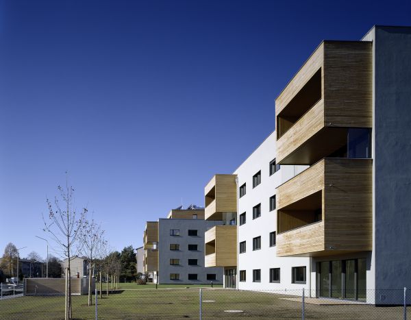 Würfelförmiges Passivhaus mit überdachten Balkonen an jeder Ecke der vier Stockwerke und Solarzellen am Dach