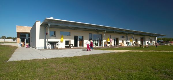 Quaderförmig gebauter, weißer Passivhauskindergarten, Kinder und ein kleiner Spielplatz