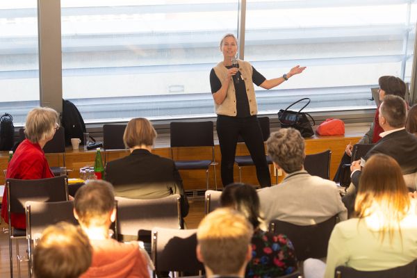 Vortragende steht vor Publikum und spricht in ein Mikrofon