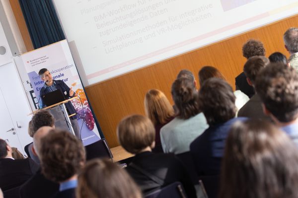 Vortragender auf dem Podium vor Publikum im Saal