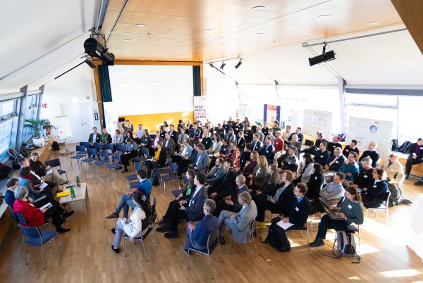 Fünf Personen sitzen in der Diskussionsrunde auf dem Podium, das Publikum sitzt halbkreisförmig darum herum